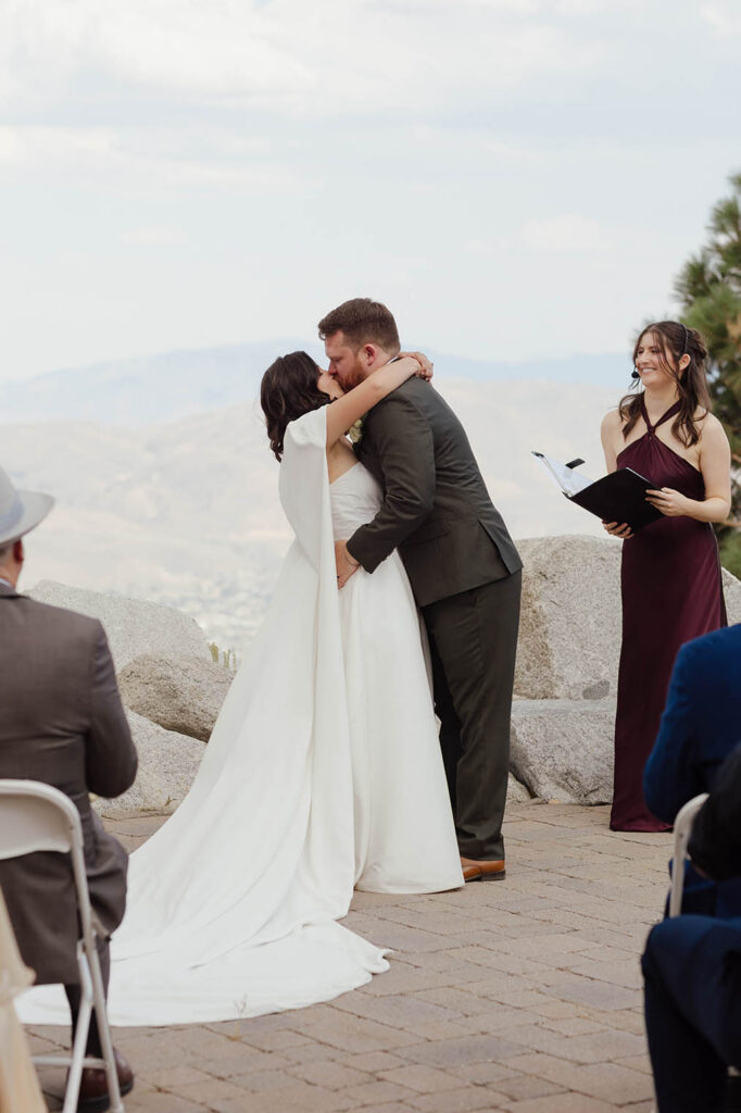 Bride and groom sharing their first kiss at Winters Creek Lodge as the officiant smiles beside them