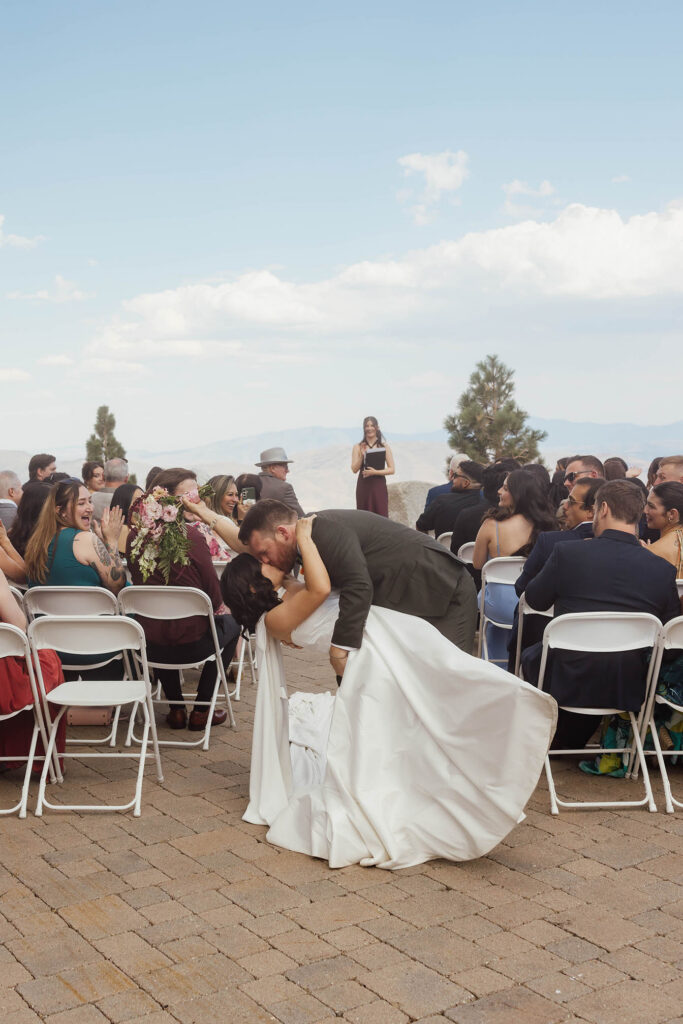 Groom dipping the bride for a kiss in the aisle as wedding guests cheer at Winters Creek Lodge