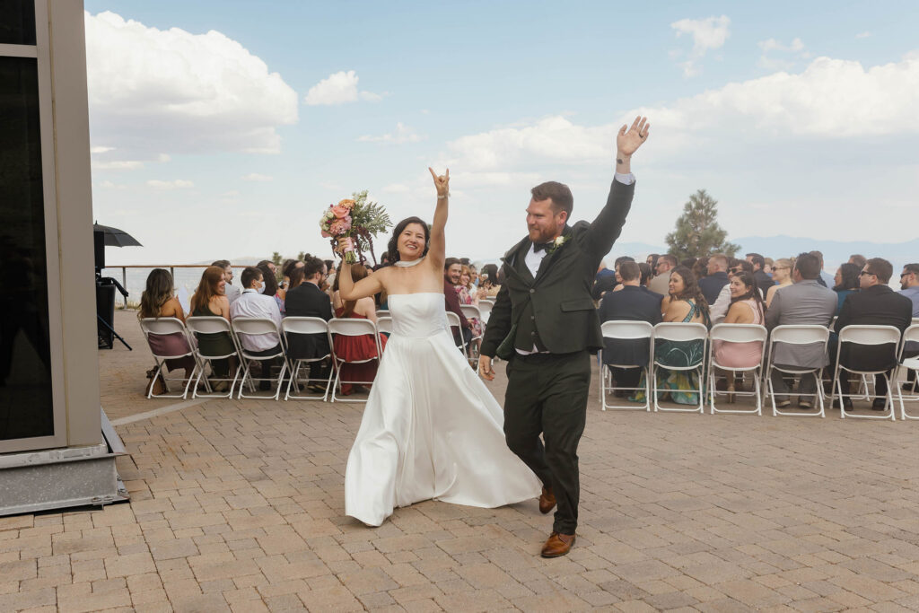 Bride and groom celebrating with raised arms as they walk across the ceremony terrace at Winters Creek Lodge