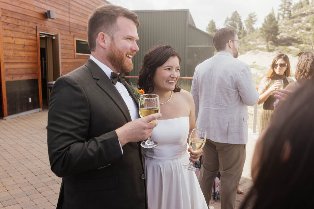 Bride and groom holding wine glasses and laughing with guests on the terrace at Winters Creek Lodge