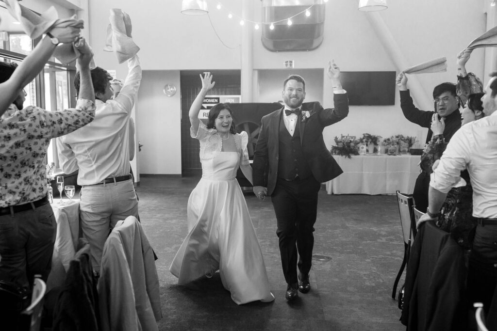 Black and white photo of the bride and groom entering their Winters Creek Lodge reception as guests wave napkins overhead