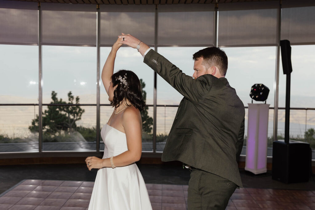 Groom twirling the bride on the dance floor beside the panoramic windows at Winters Creek Lodge