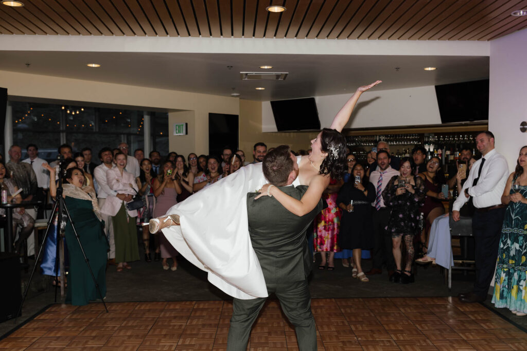 Groom lifting the bride during their wedding dance as she raises an arm and guests cheer around them at Winters Creek Lodge