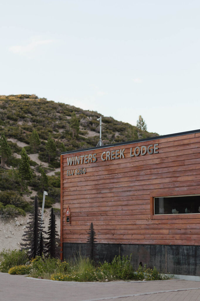 Wood exterior of Winters Creek Lodge near Lake Tahoe with the venue name and elevation sign beneath a mountain hillside